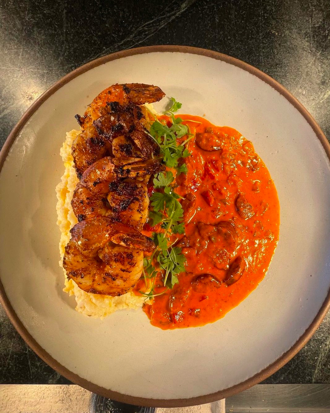 Grilled shrimp over a pale creamy base beside orange-red sauce with sliced mushrooms and microgreens