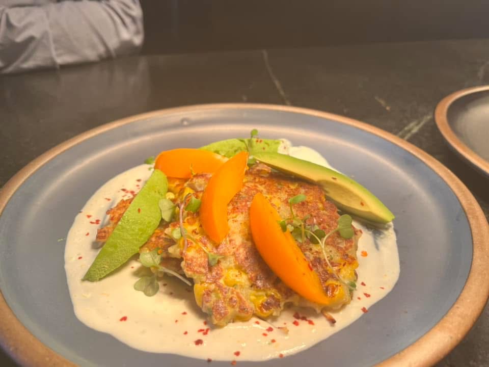 Golden savory cakes with avocado slices, orange wedges and microgreens over a creamy sauce