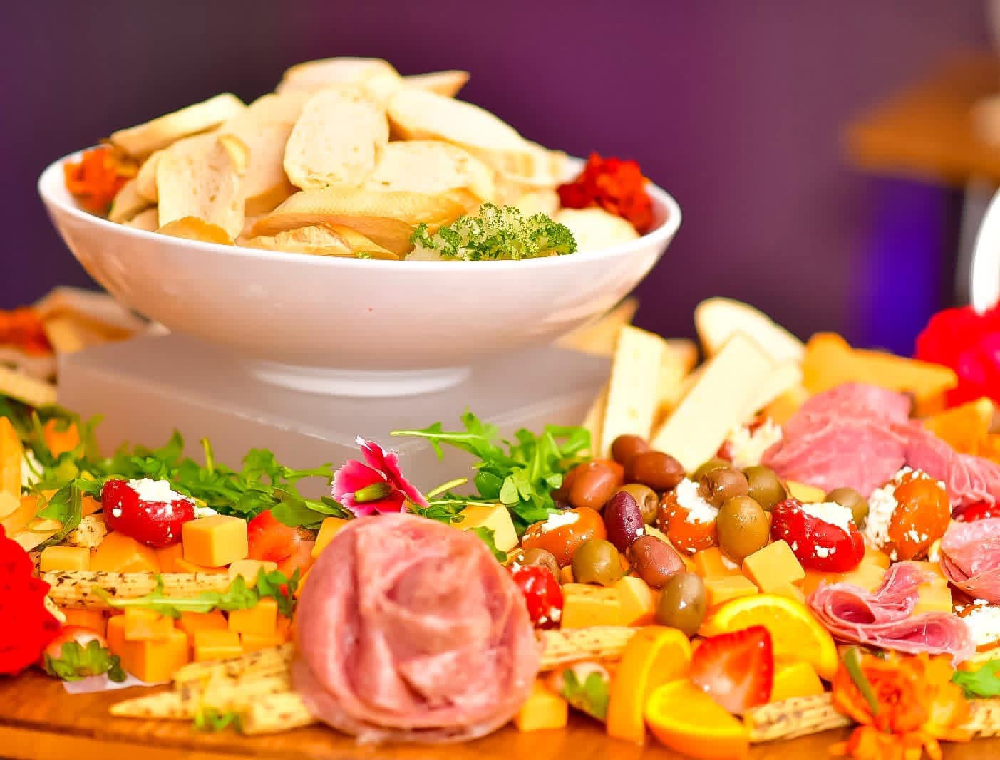 Grazing display with sliced bread, cured meats, cheese, olives and colorful garnishes