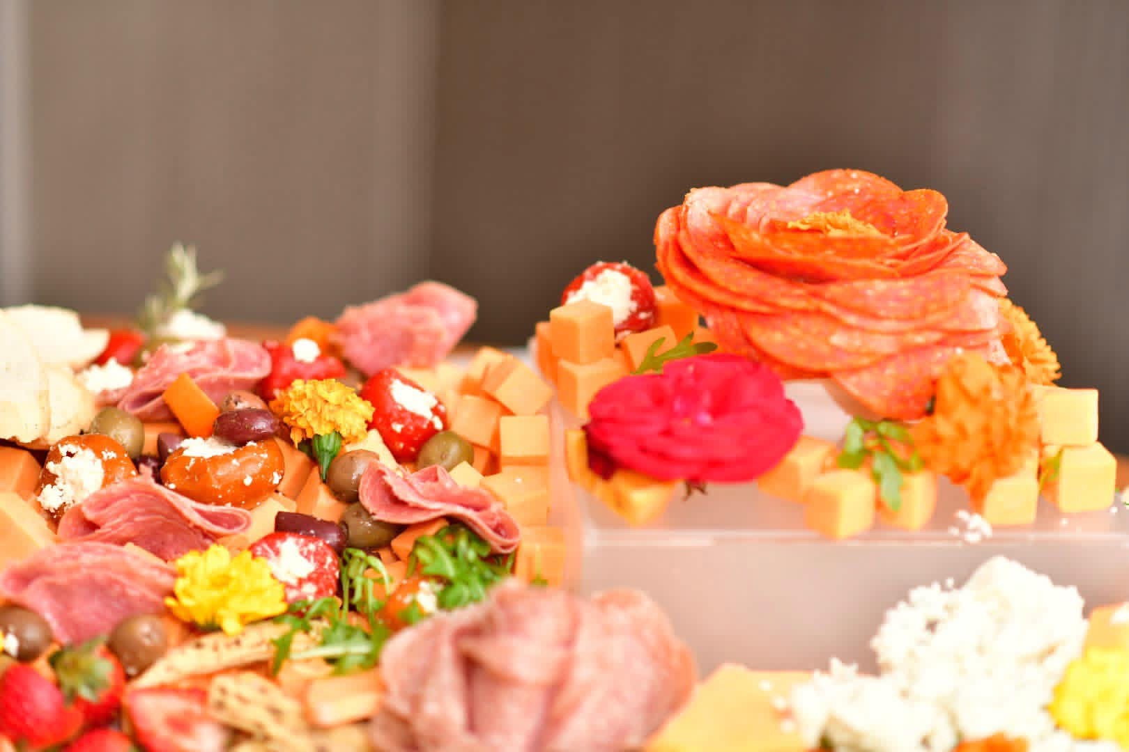 Cured meat roses surrounded by cheese, olives, tomatoes and flowers