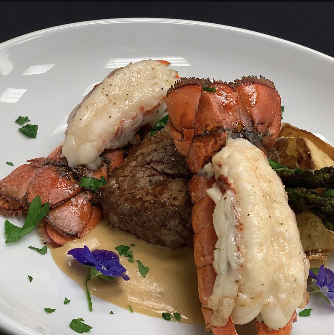 Close-up of lobster tails and steak with sauce, vegetables and edible flowers