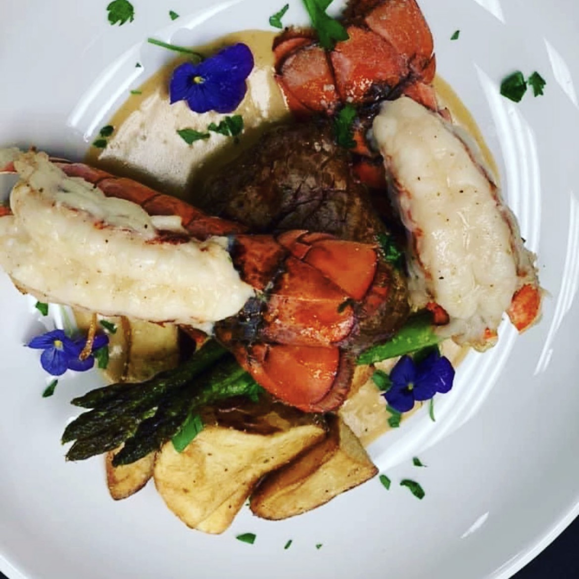 Overhead view of lobster tails and steak with asparagus, potatoes and edible flowers